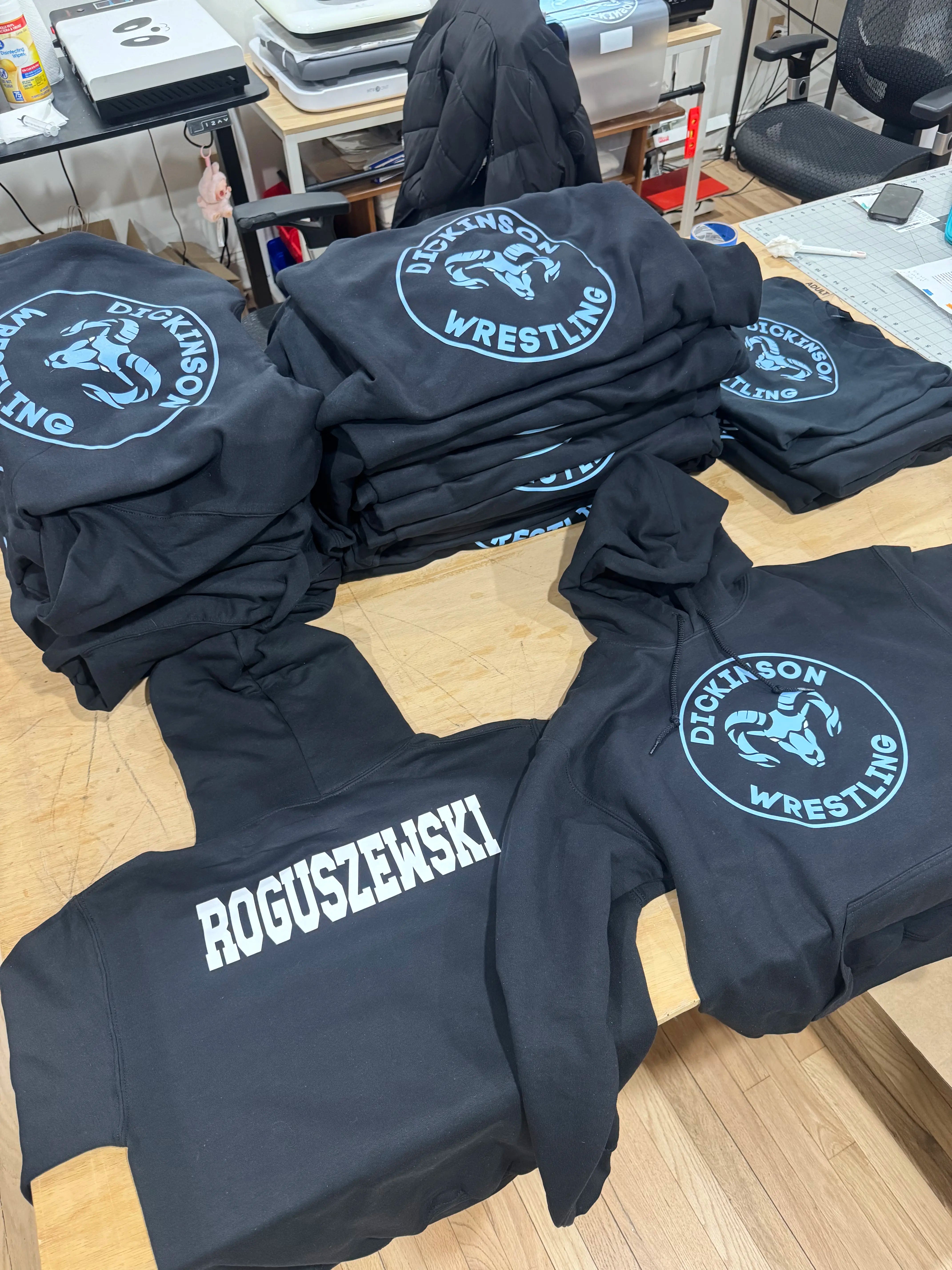 Stacks of black t-shirts with 'Dickinson Wrestling' logo on a wooden table.