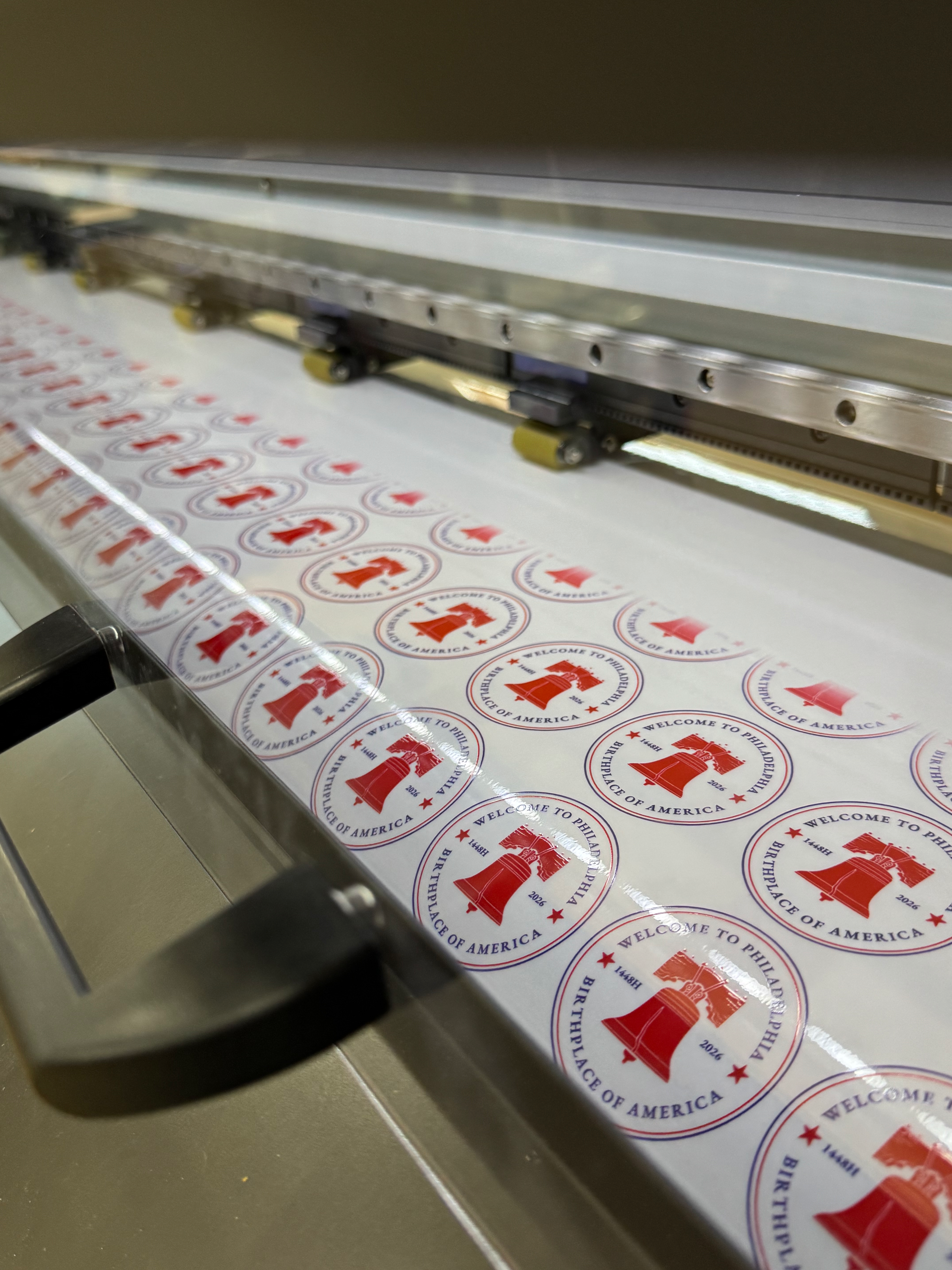 Sheet of printed labels with red and blue graphics on a printing machine.