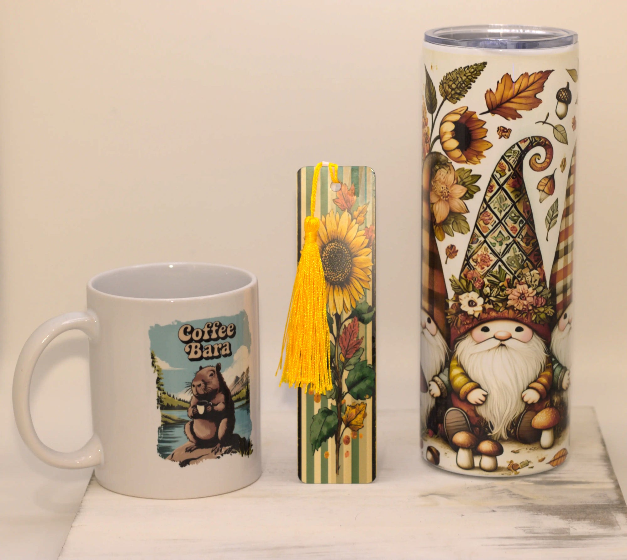 Mug, bookmark, and tumbler with autumn-themed designs on a light background