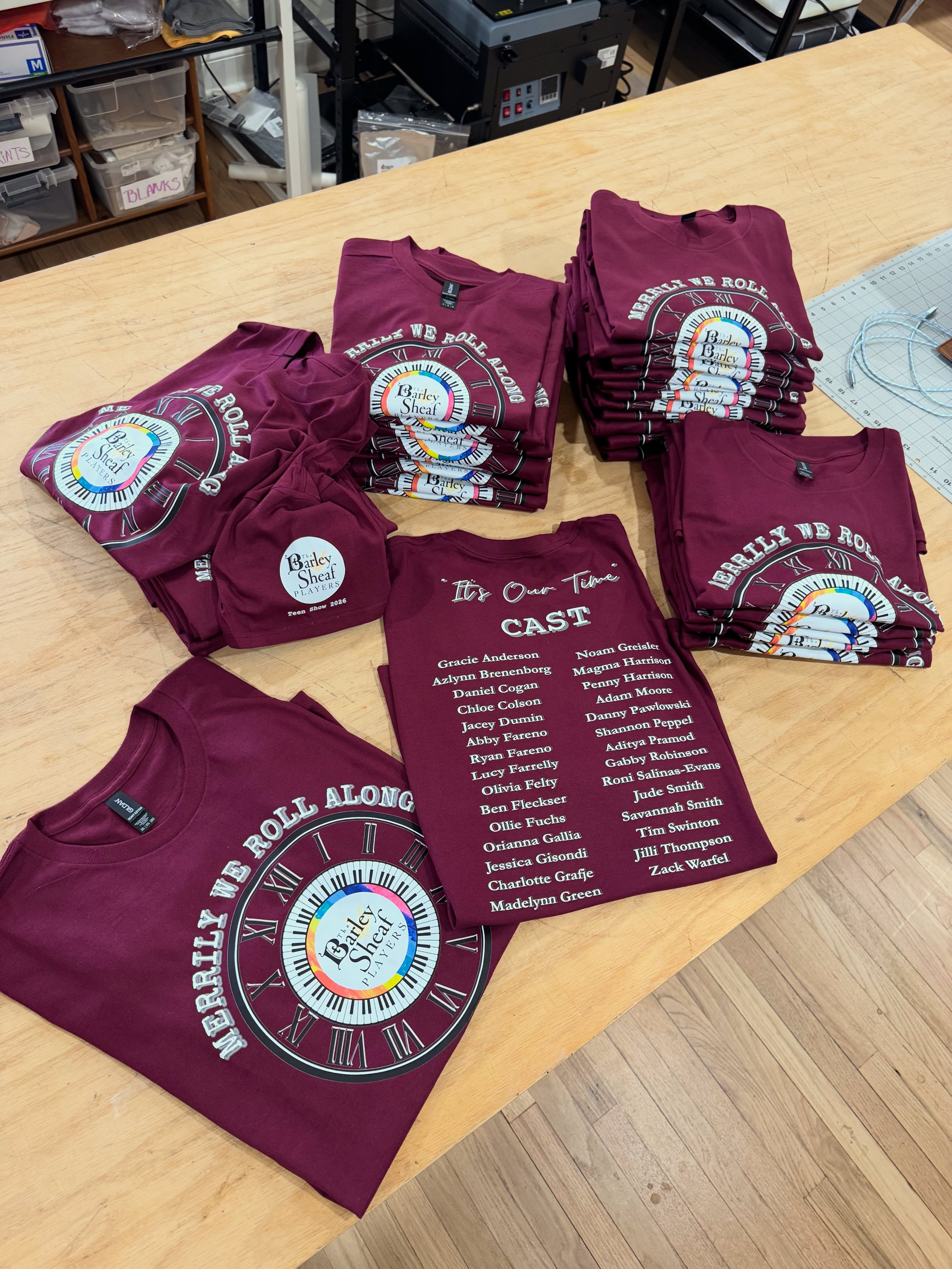 Maroon custom printed t-shirts with text and graphics on a wooden table